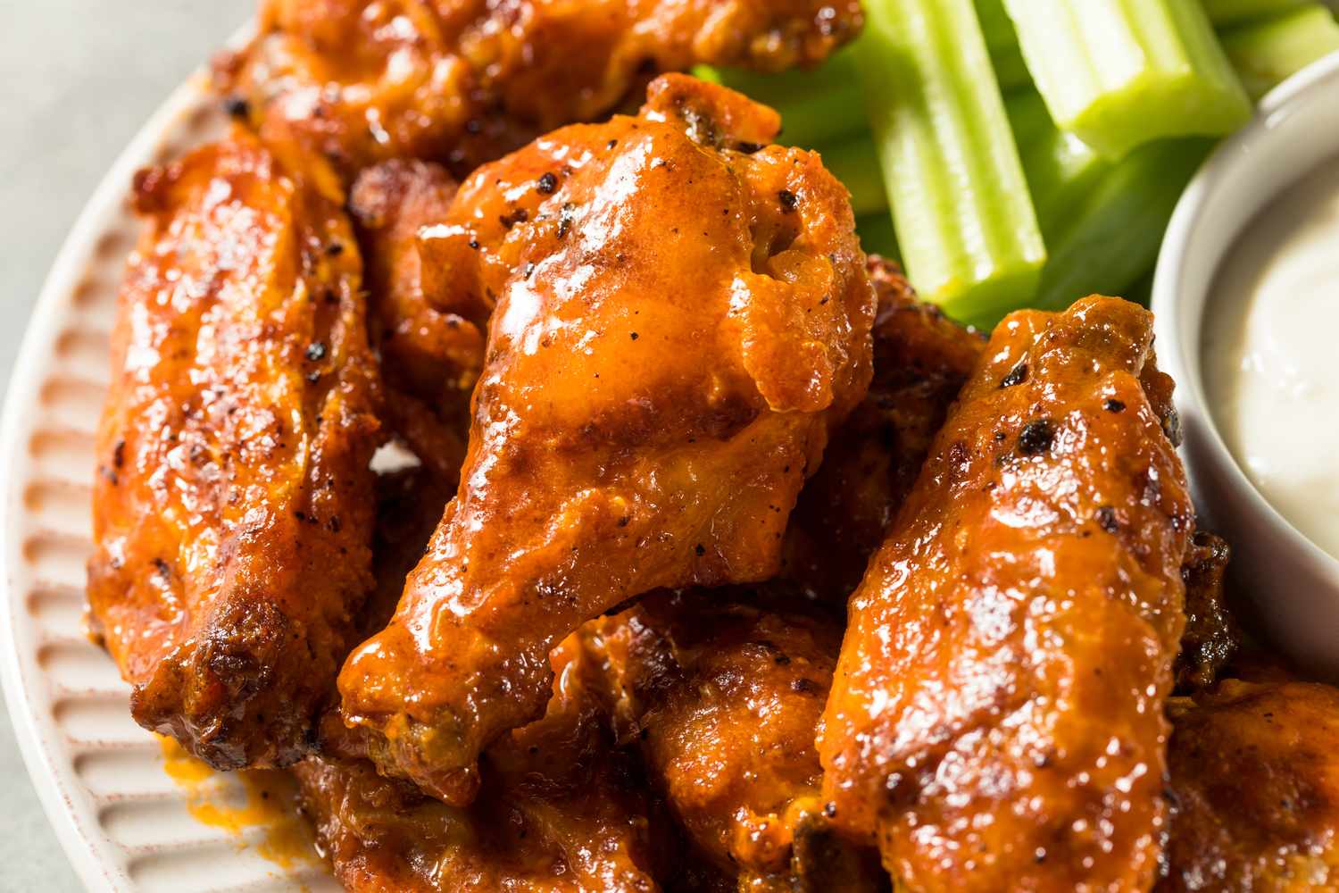 Buffalo chicken wings on a plate with celery sticks and a bowl of dip
