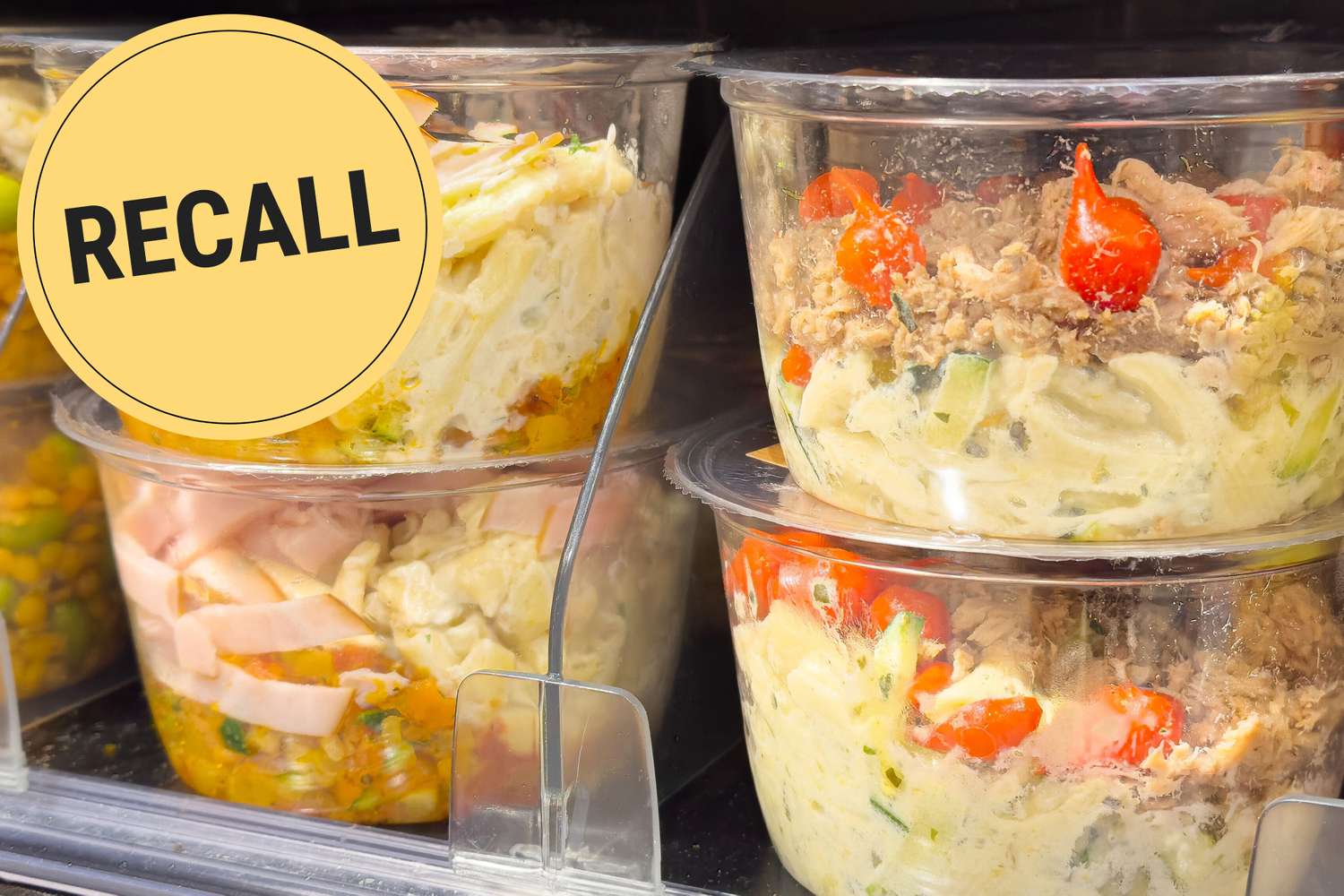Packaged pasta salad in containers displayed in a refrigerator with a Recall label overlay