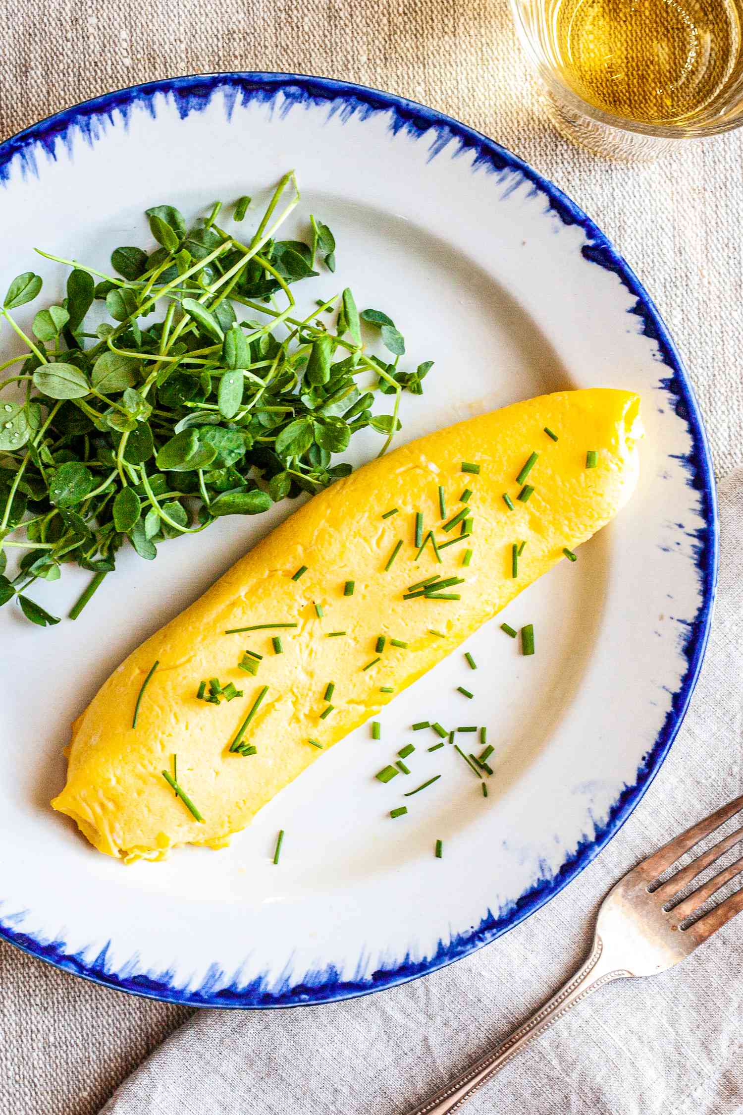 French Omelette with Greens on Plate Next to Glass and Fork