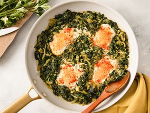 A pan of Nargesi a Persian dish with eggs cooked atop seasoned sauted greens displayed on a countertop next to utensils