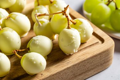 Closeup view of white chocolate covered green grapes on a wooden cutting board on a gray countertop