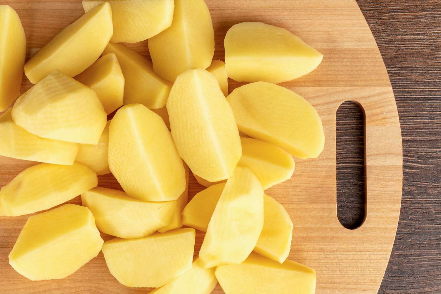 Peeled and cut potatoes on a wooden cutting board with a handle