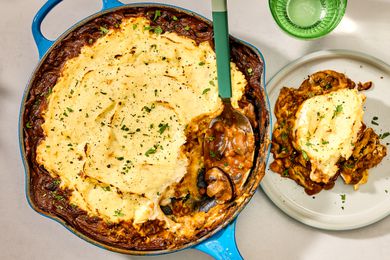 Overhead shot of lentil shepherd's pie in a skillet, with a serving spoon having scooped a serving of the dish out on a plate to the right of the skillet