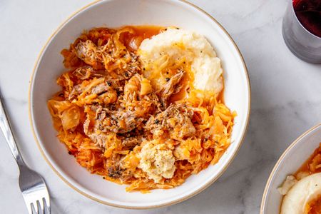 Braised pork roast served over sauerkraut with a side of mashed potatoes in a bowl