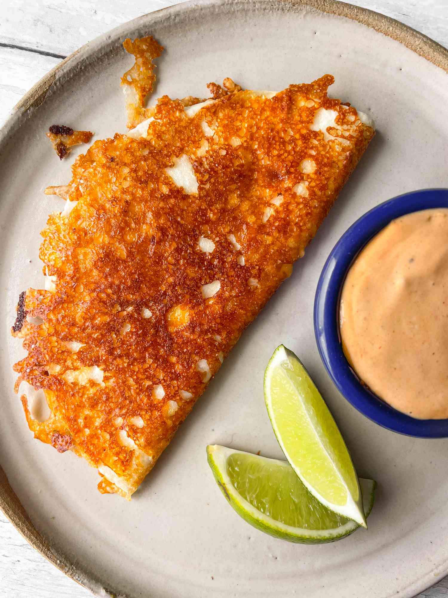 Burnt Cheese Taco on a Plate with Chipotle Sauce and Lime Wedges
