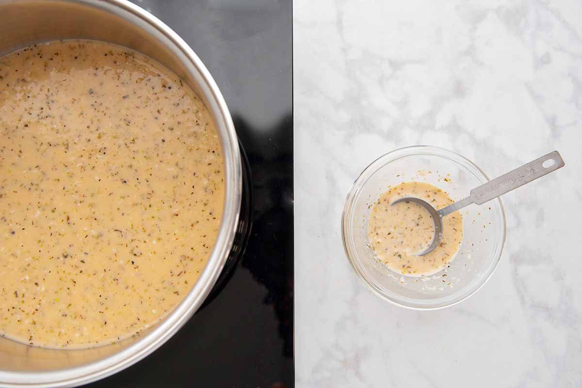 Mojo marinate in a sauce pan. A small glass bowl with thickened marinade and a tablespoon rest on a marble background to the right.