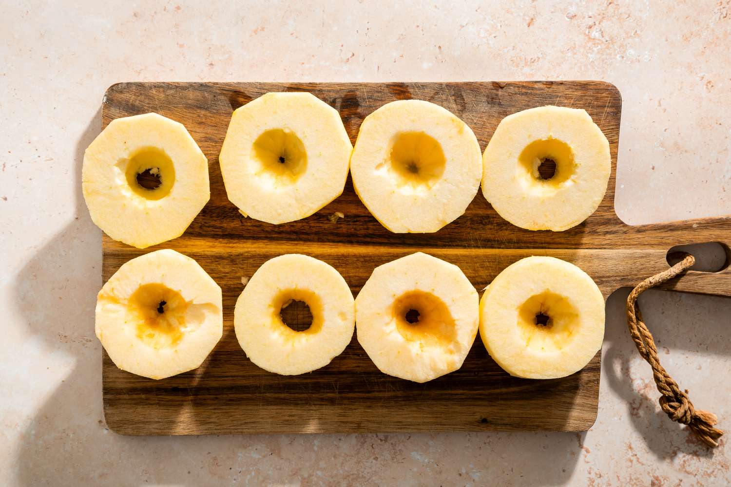A wooden board with eight cored apple slices arranged in two rows