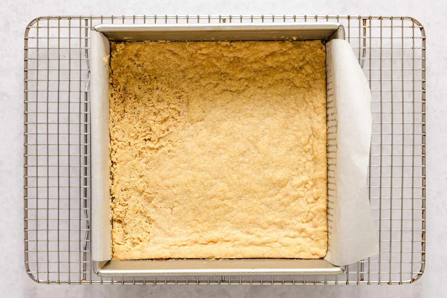 A square baking tin containing a golden crust layer for caramel apple bars recipe on a cooling rack