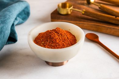 Small bowl of chili powder on a counter with measuring spoons and a small spoon