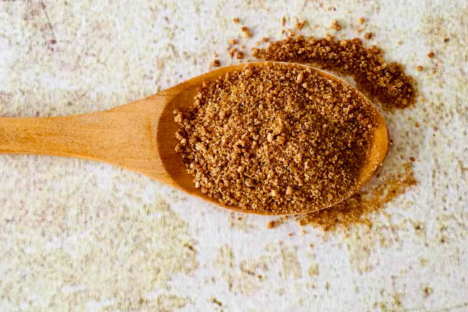A wooden spoon holding granulated coconut sugar