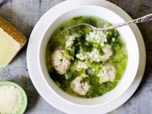 Italian wedding soup with meatballs in a white bowl and parmesan on the side