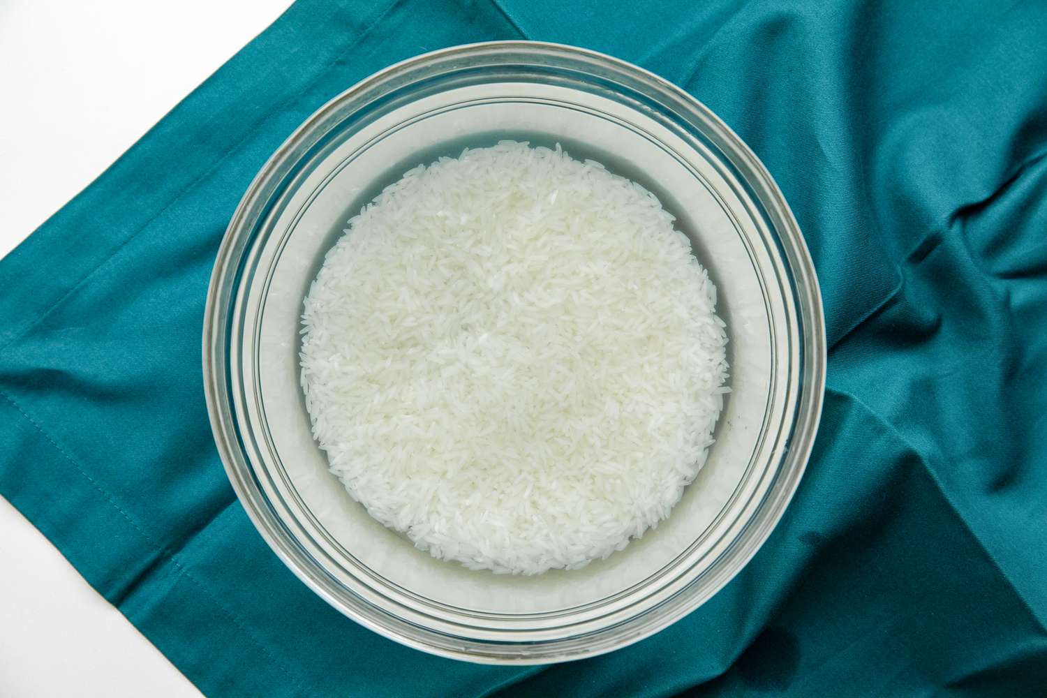 Washing Rice: Rice in a Bowl of Clear Water on a Teal Kitchen Linen for Chicken Jook Recipe
