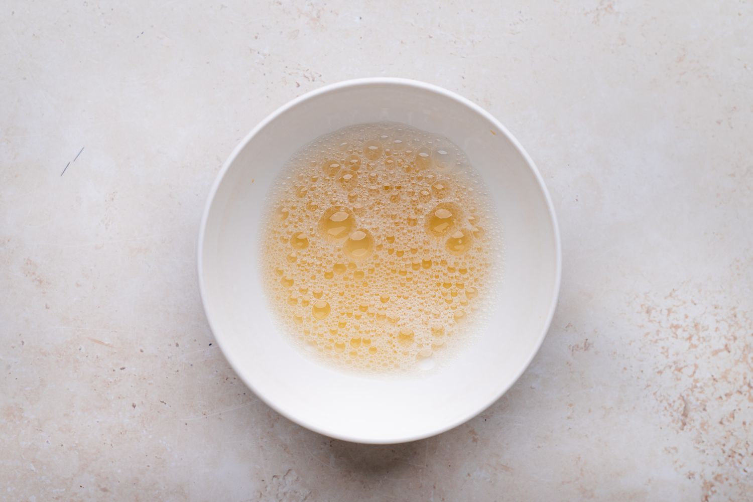 A small bowl of egg white, water, and vanilla for a candied pecan recipe.