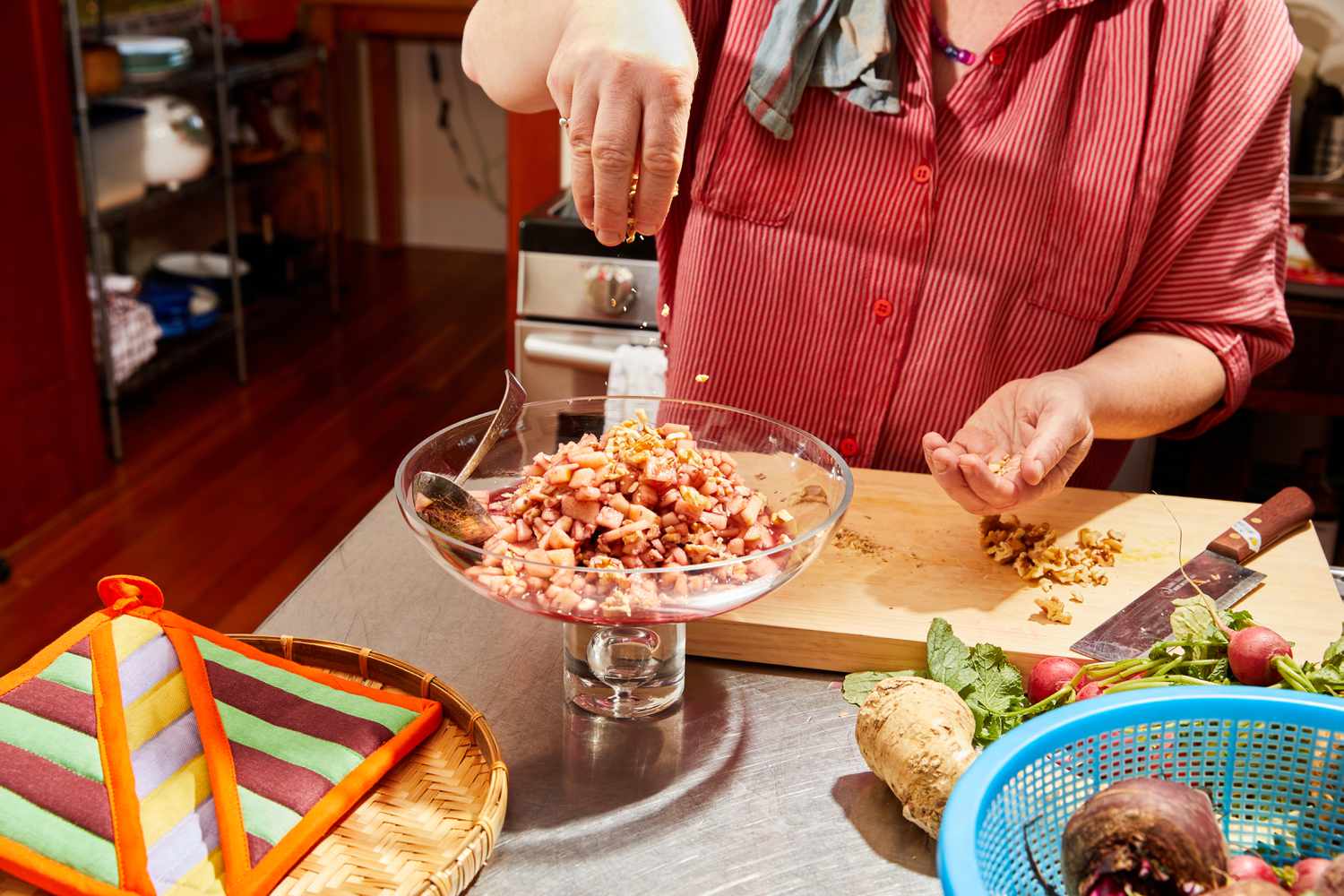 A hand sprinkling walnuts over a glass dish or charoset