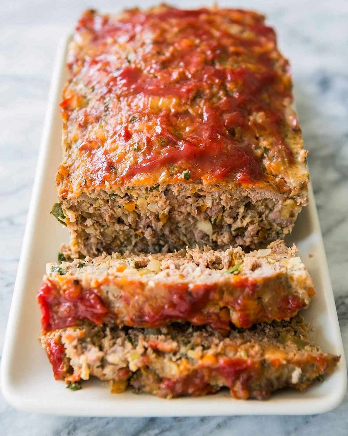 Sliced meatloaf topped with a tomato glaze on a rectangular white serving plate