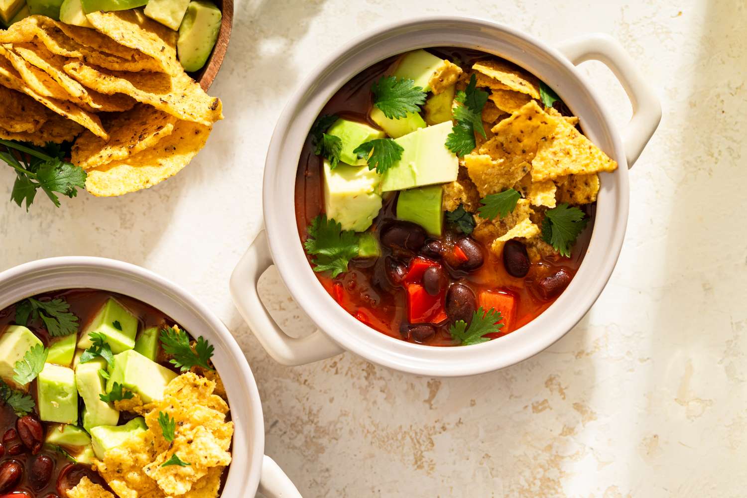 Bowls of tortilla soup garnished with avocado tortilla chips and cilantro