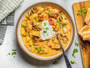 Bowl of Chipotle Chicken Chowder Next to a Wooden Board with Baguette Pieces and Table Napkin