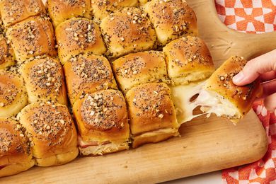 Funeral Sandwiches on a serving board, one sandwich being pulled by a hand, delicious looking cheese stretch