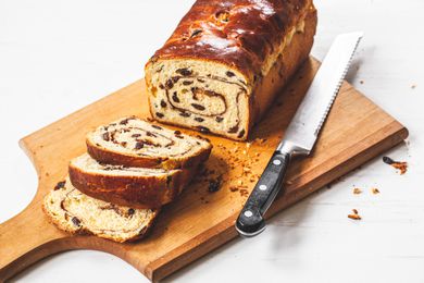 Slices of Cinnamon Swirl Raisin Brioche Loaf Next to the Remaining Loaf and a Bread Knife on a Cutting Board
