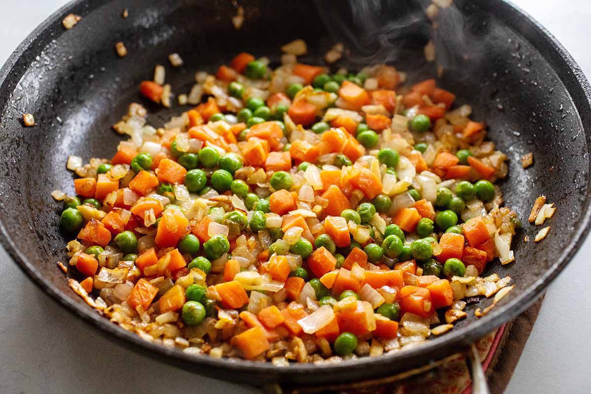 A black skillet with frozen peas and carrots sauteing inside.