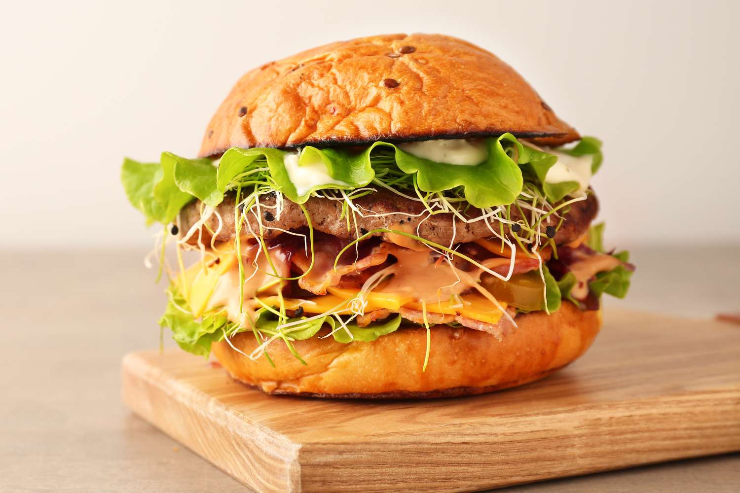 A gourmet burger with lettuce, sprouts, cheese, and mayo on a wooden surface