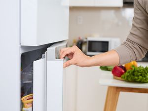 A young man opening a refrigerator door in a kitchen with a microwave visible in the background