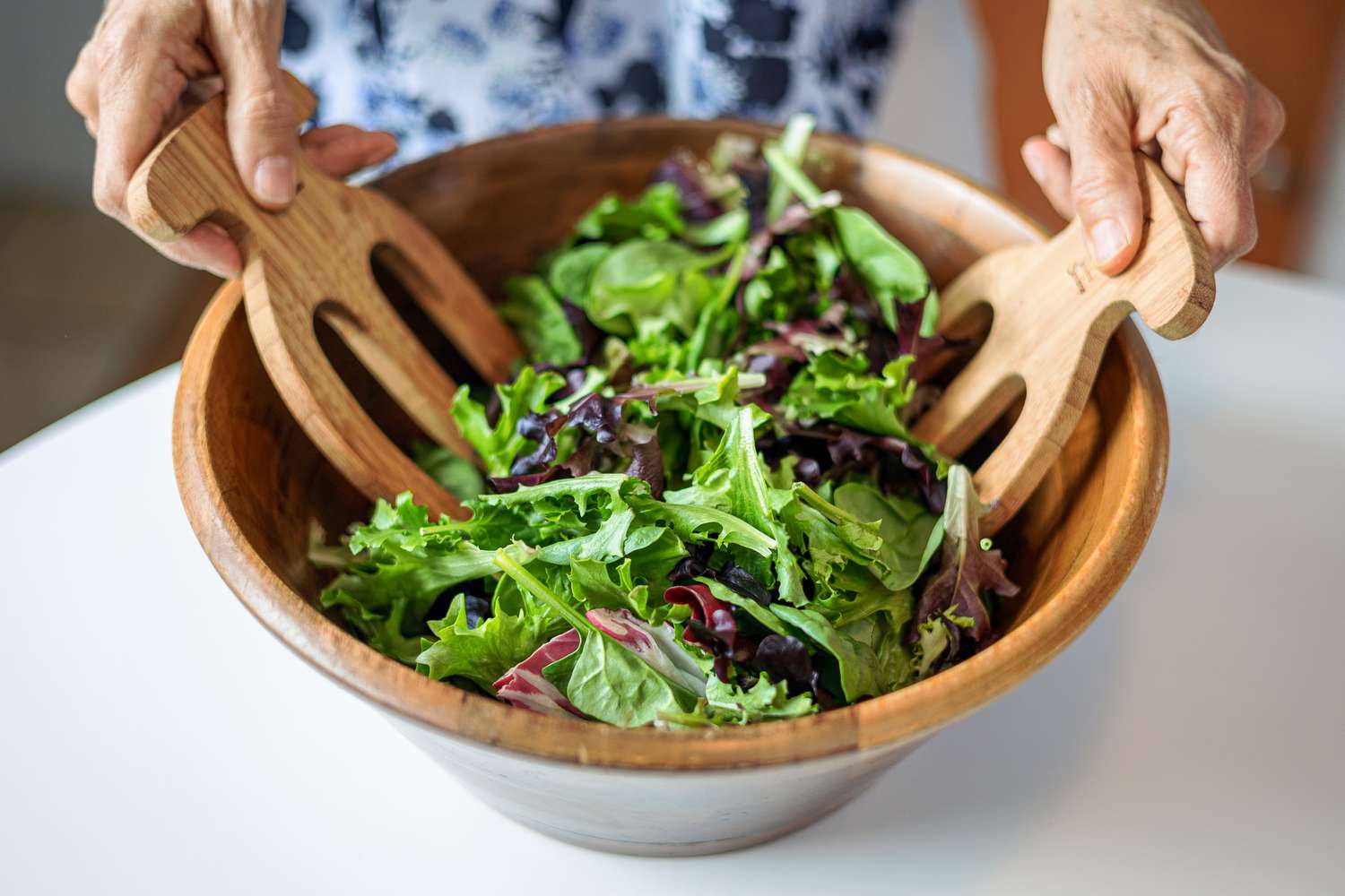 Mixed slad greens getting tossed together in a wooden bowl