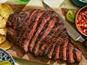 Sliced carne asada fanned out on a cutting board with salsa and tortillas nearby
