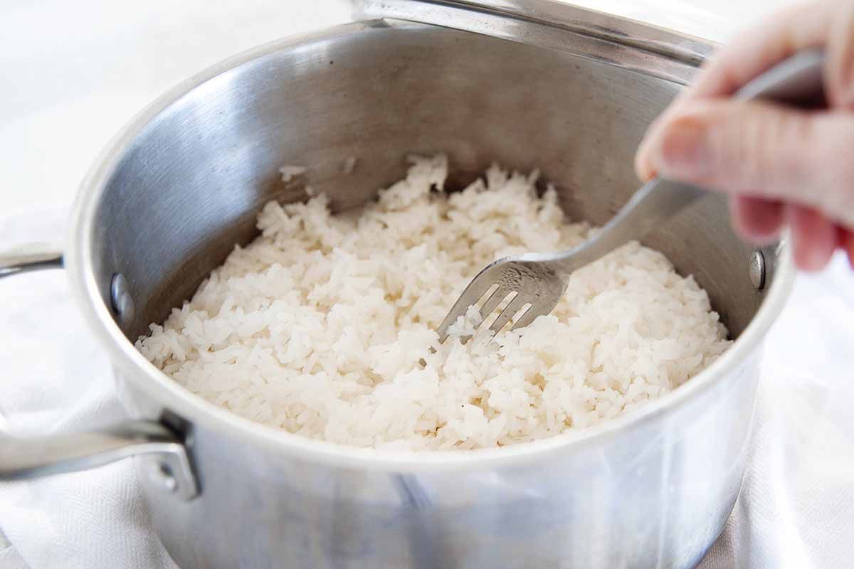 Silver saucepan with perfect white rice being fluffed with a fork.