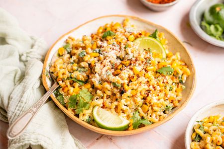 A bowl of esquites pasta salad garnished with lime wedges and cilantro