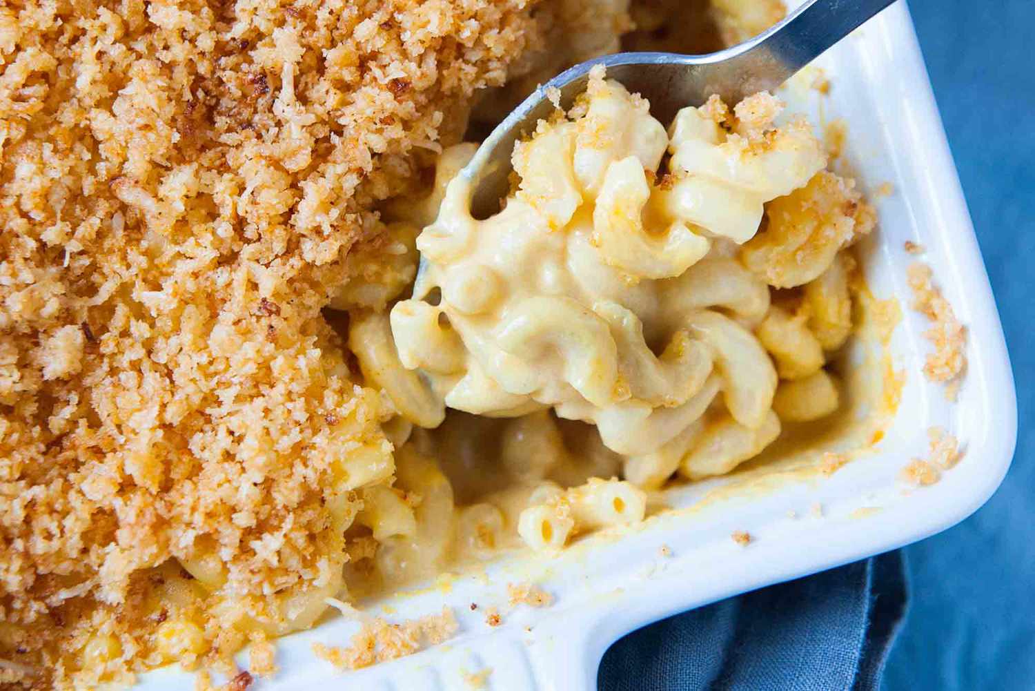 mac and cheese topped with bread crumbs in a baking dish a spoon removing a serving