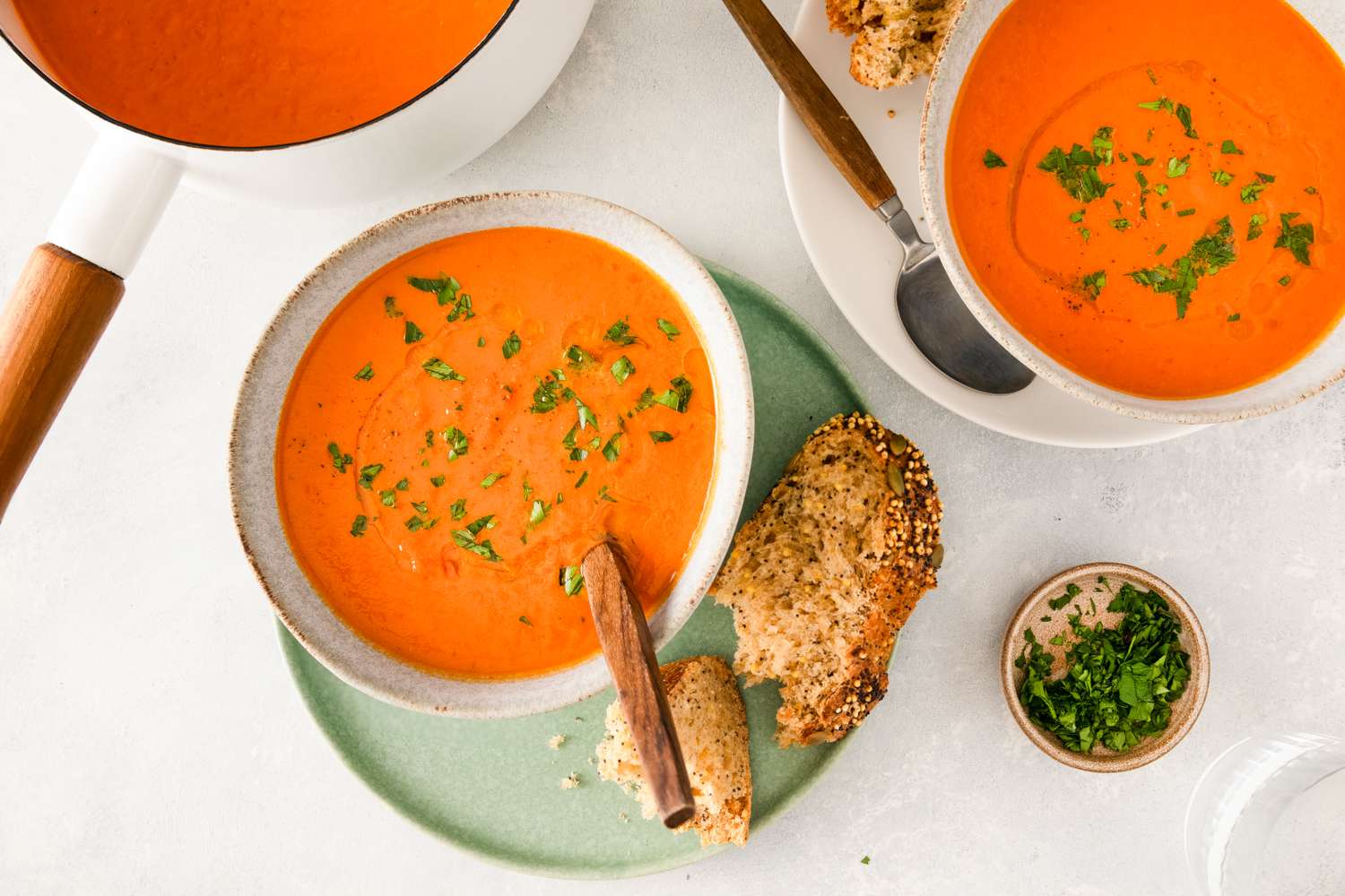Bowls of pumpkin tomato soup with bread on the side garnished with herbs