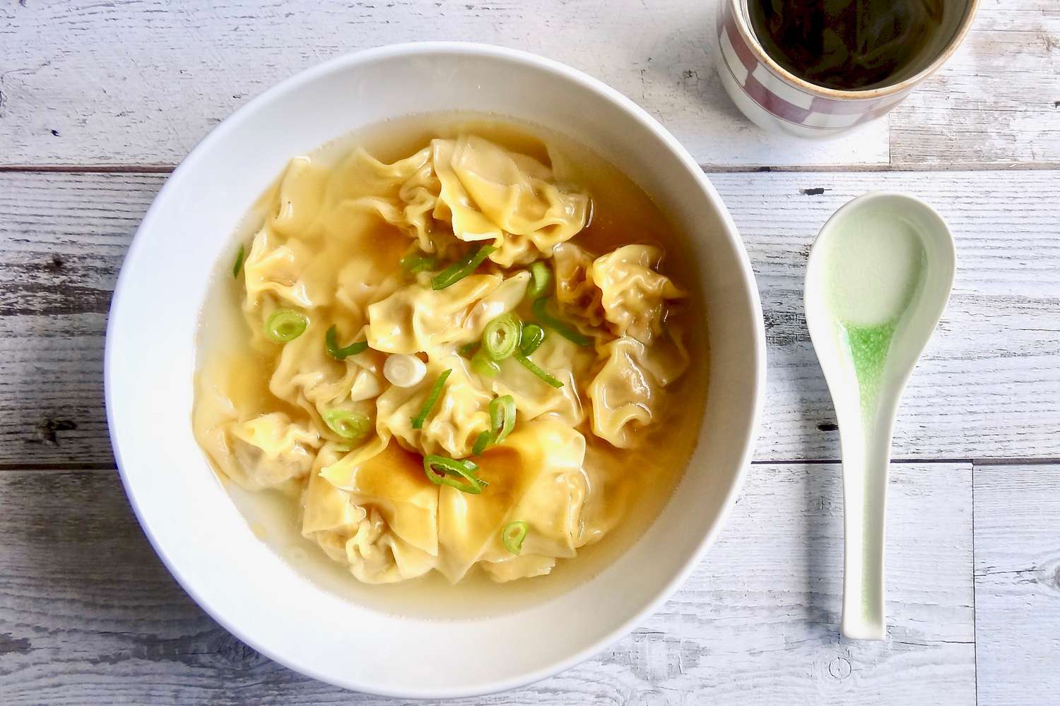 Overhead view of a bowl of pork and ginger wontons in chicken soup.