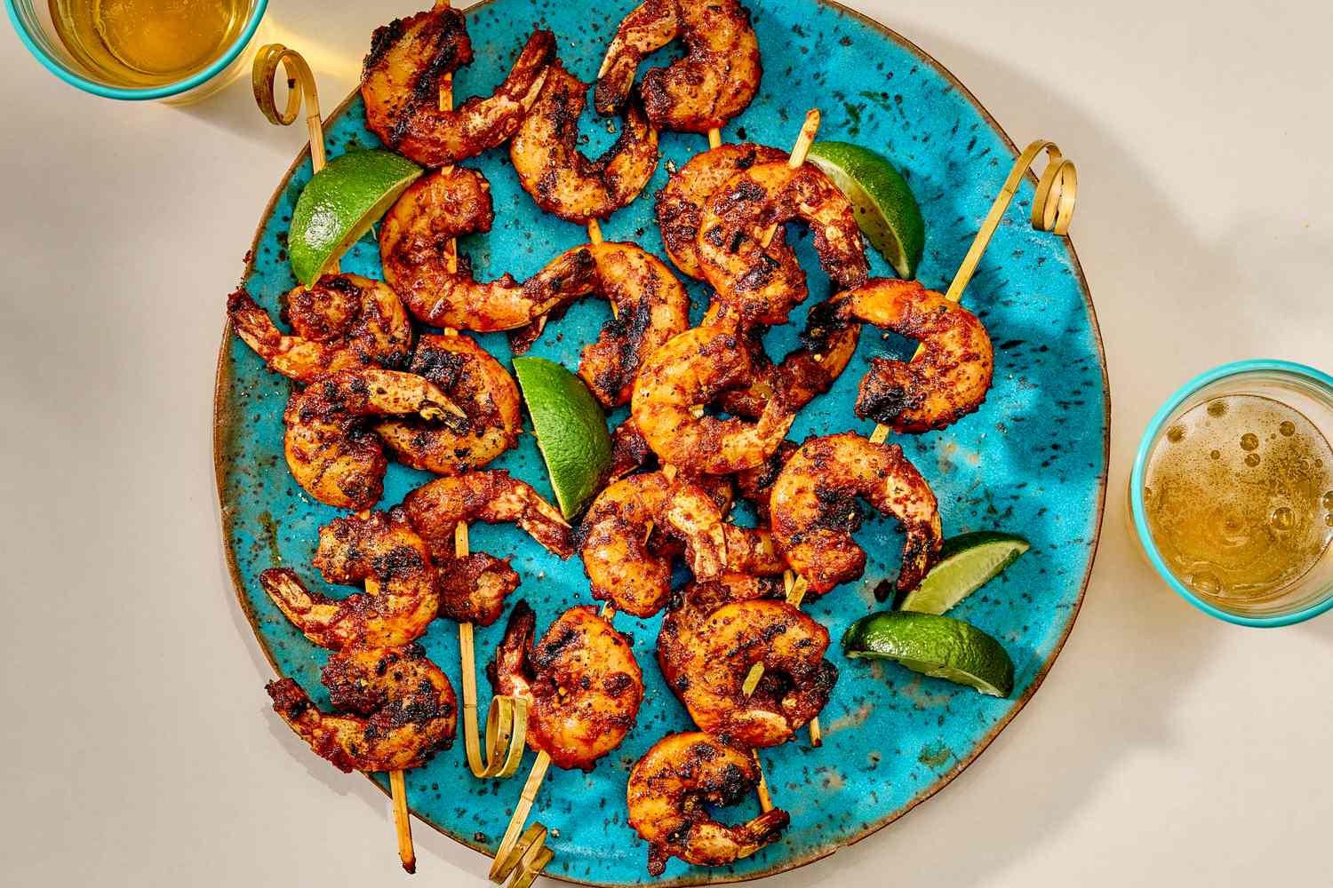 Platter of shrimp skewers with lime wedges, served on a blue plate accompanied by drinks