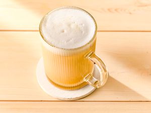A mug of coffee with foam on top placed on a coaster on a wooden surface