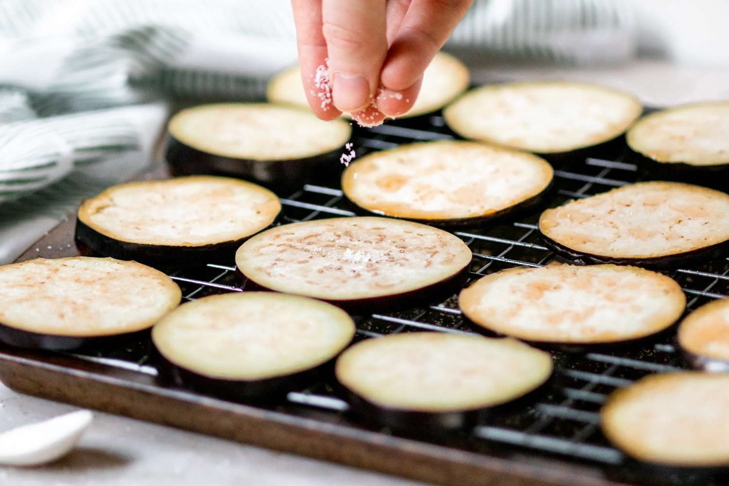Sprinkling sliced eggplant with salt to make eggplant parmesan.