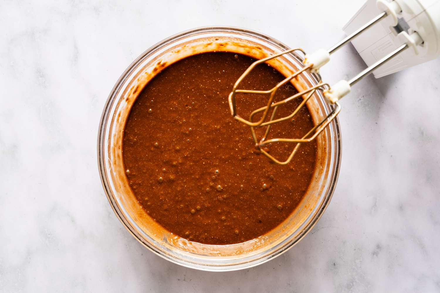 Glass bowl containing cake batter with a handheld mixer for Italian love cake recipe