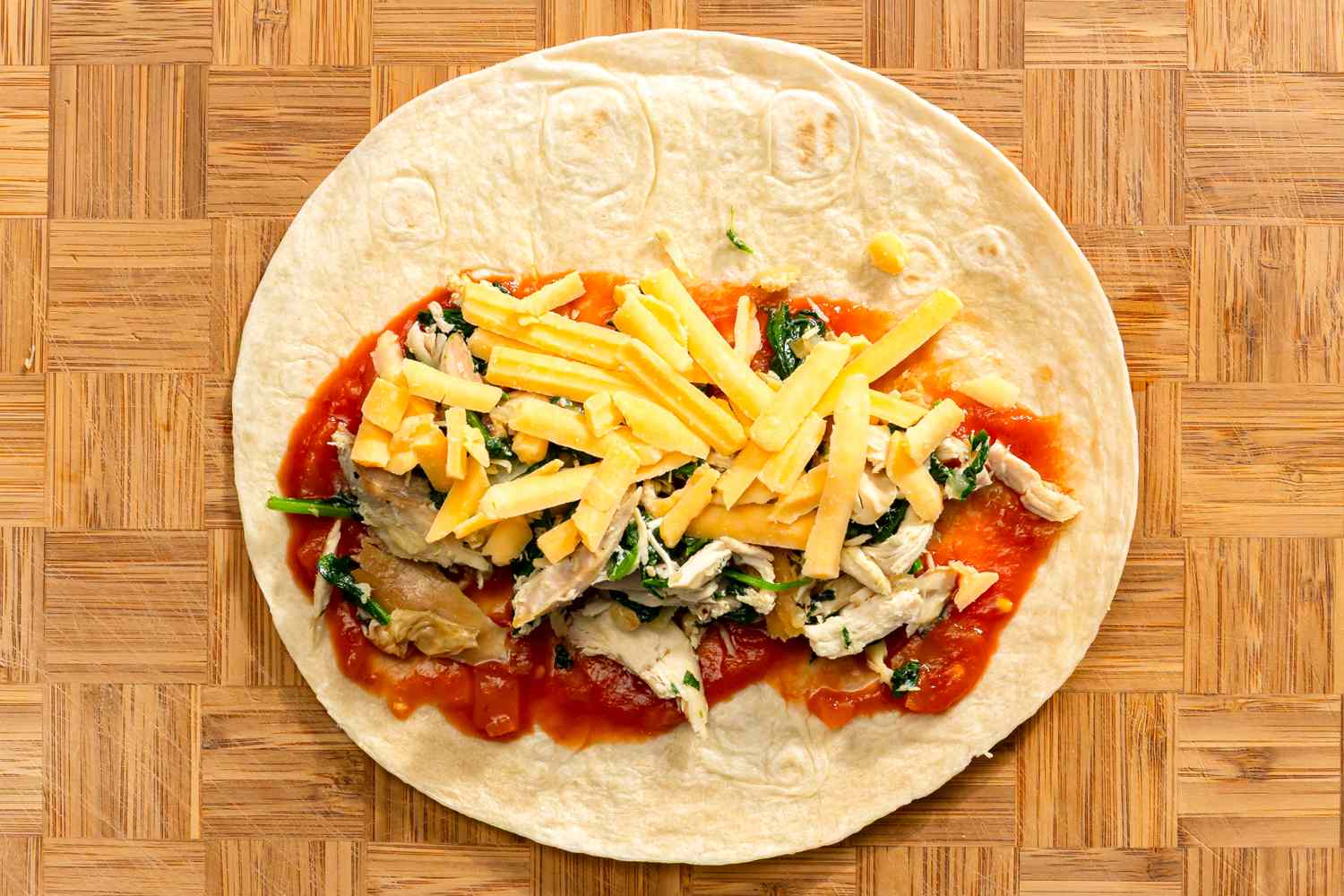 Tortilla topped with chicken spinach tomato sauce and grated cheese for Chicken and Spinach Tortilla Bake recipe