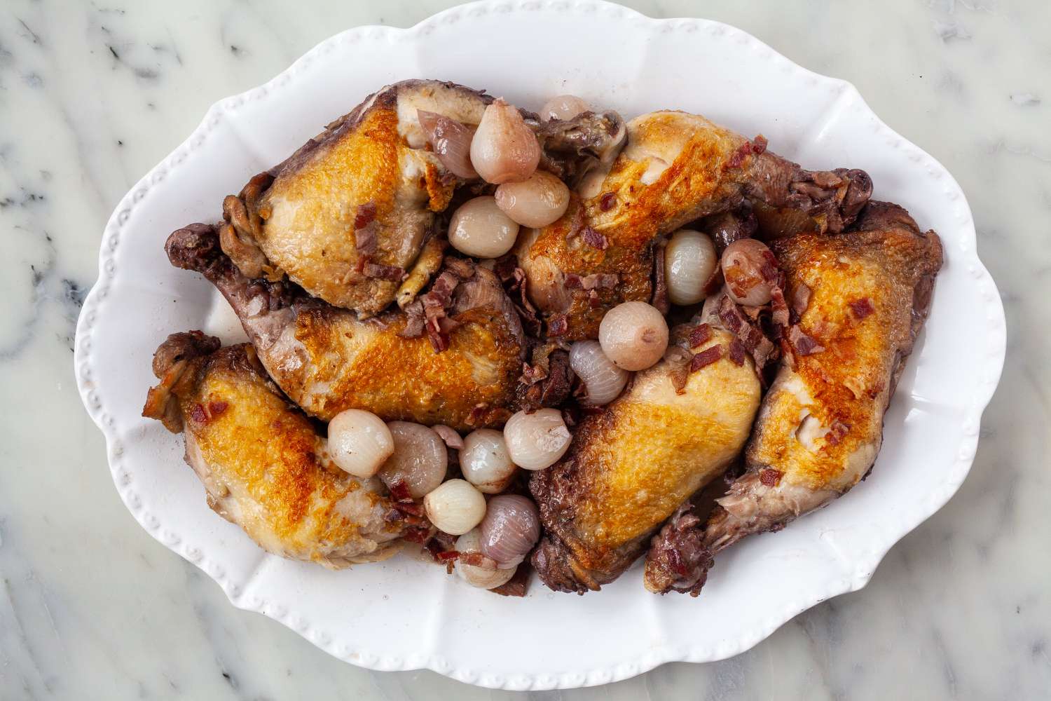 Chicken and onions removed from a platter to make coco vin.