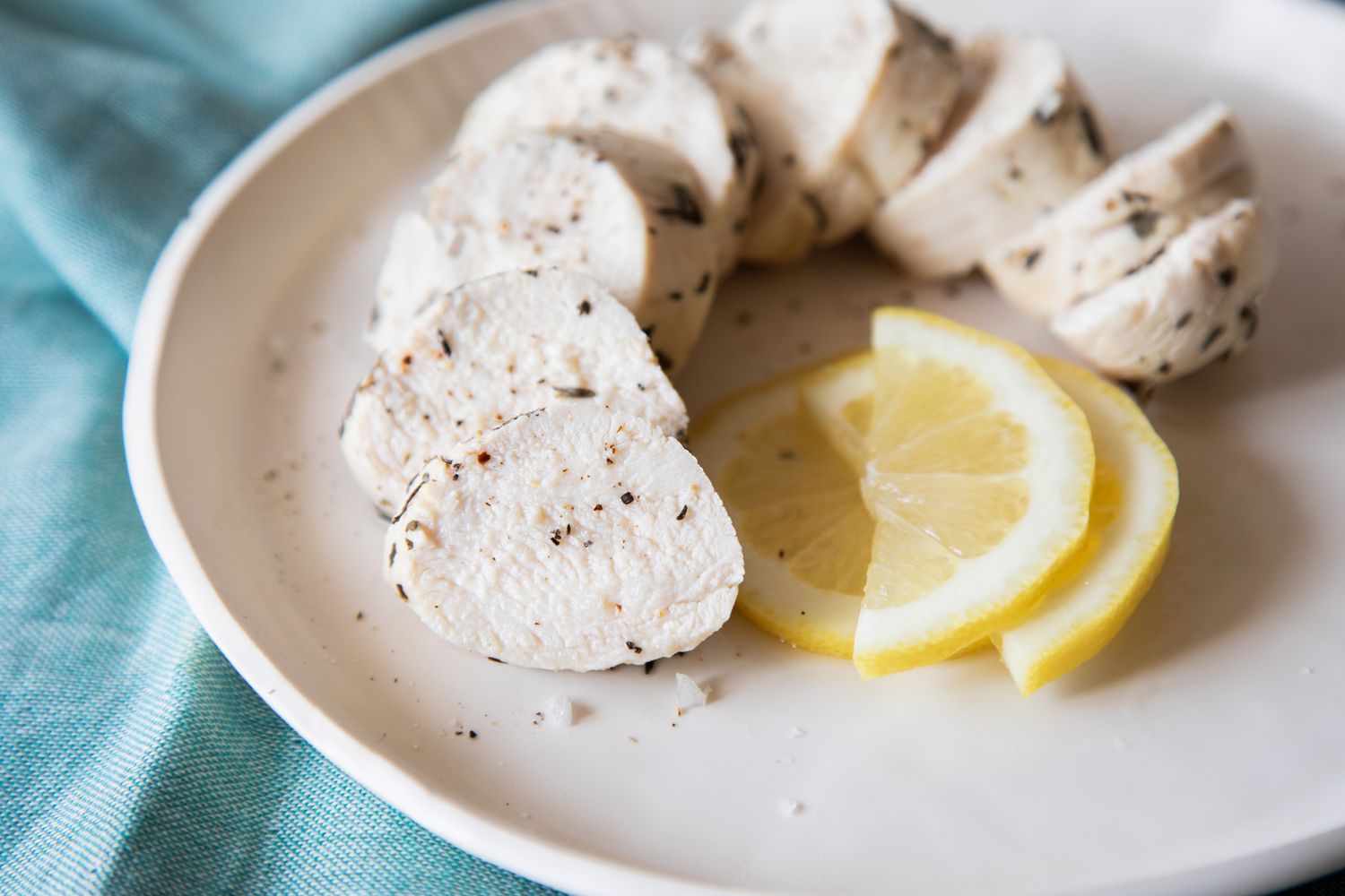 Sliced poached chicken on a plate with a lemon slice.