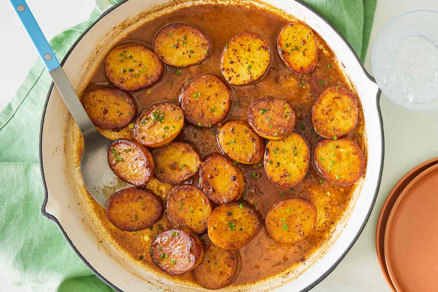 Miso melting potatoes in a skillet, with a serving spoon about to scoop some of the potato slices out