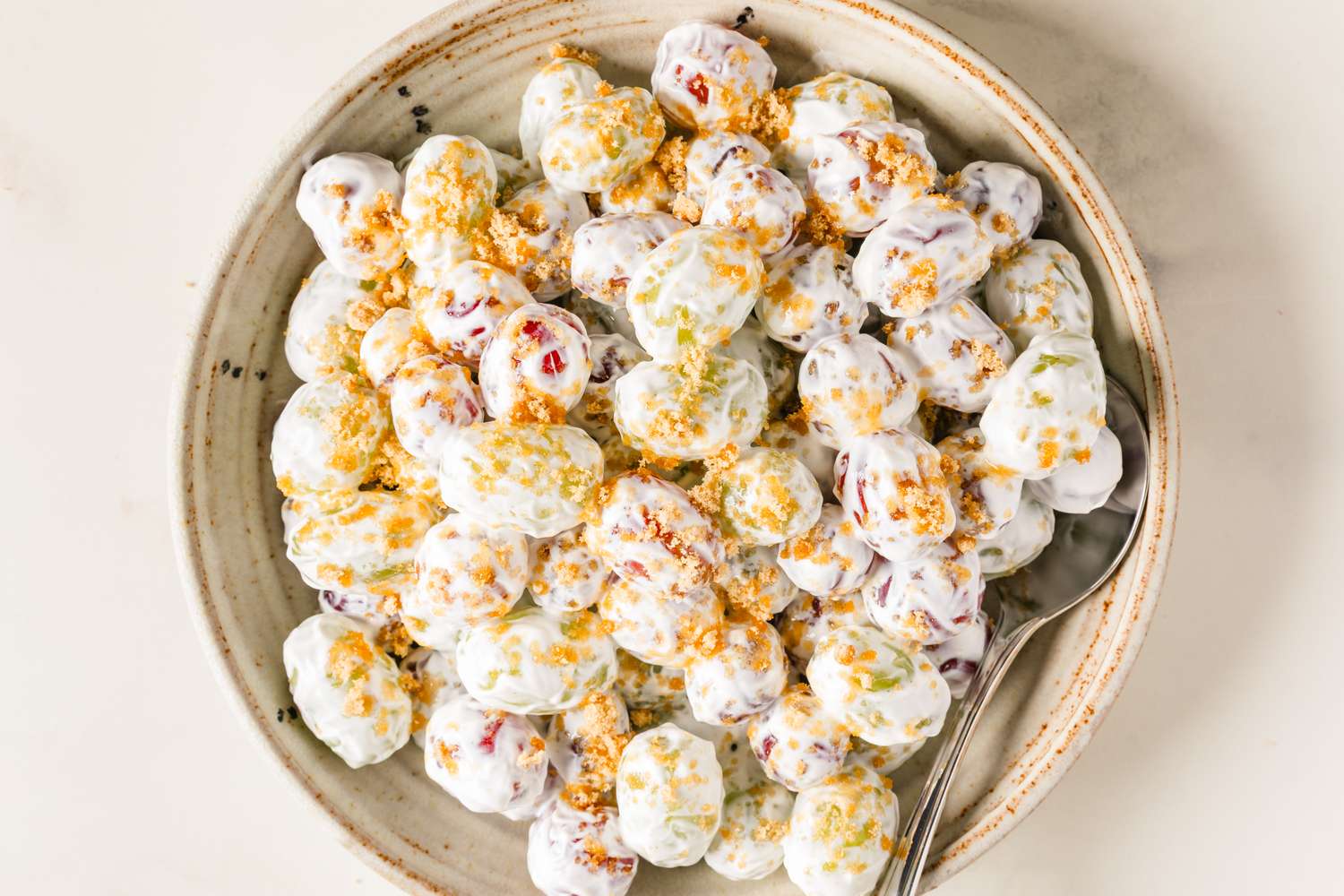 A plate of grape salad with a creamy topping and crumbled ingredients served with a spoon