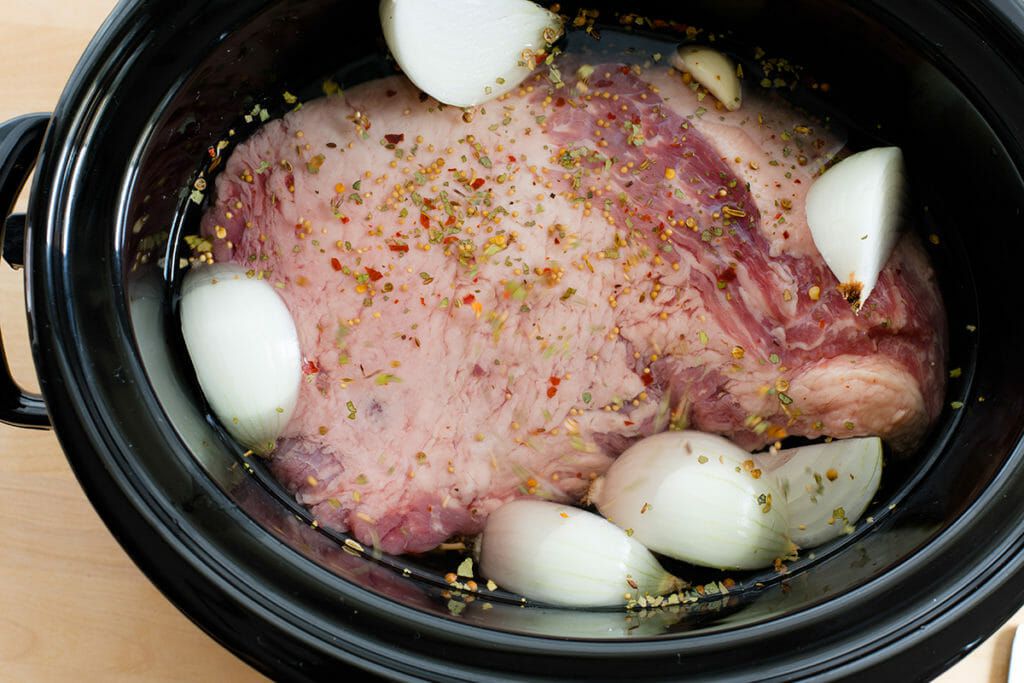 Corned Beef in the Slow Cooker raw corned beef with onion wedges in slow cooker