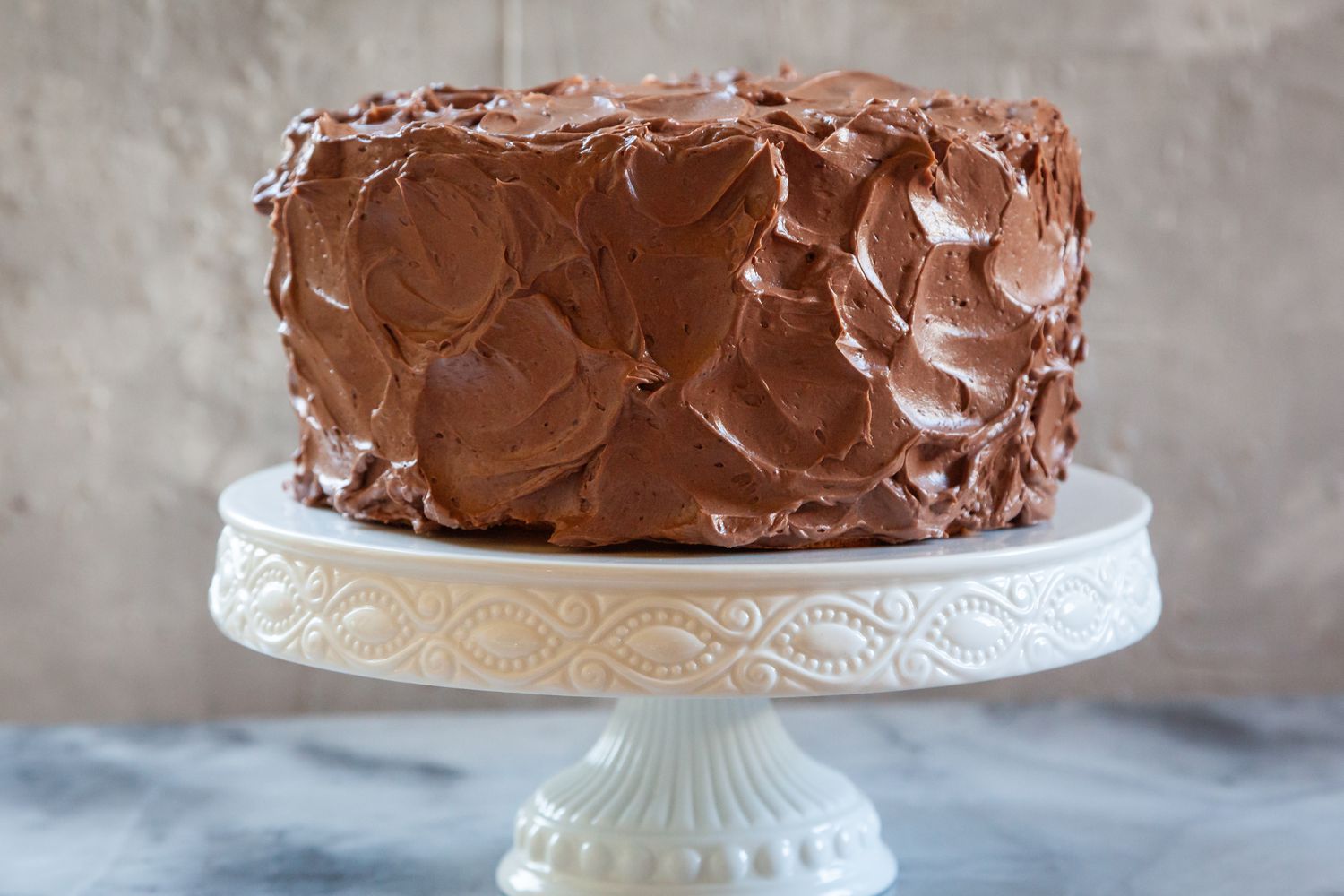 A chocolate cake on a cake stand showing a cake frosting technique.