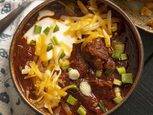 A bowl of chili with shredded cheese sour cream and green onions