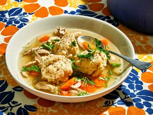 Matzo ball soup in a white bowl with a spoon on a flowered tablecloth