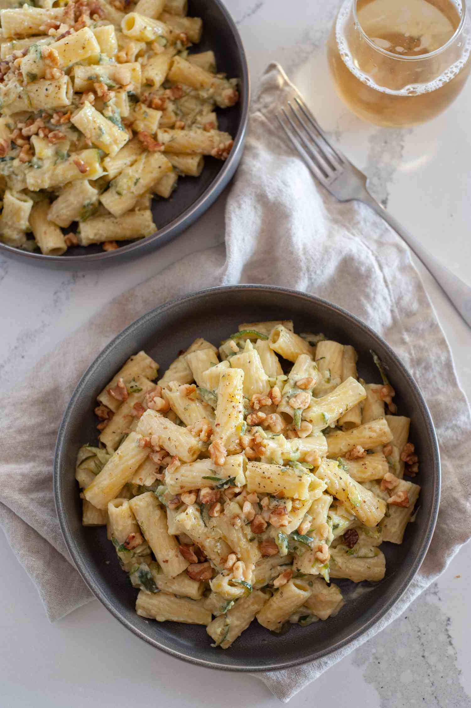 Two Bowls of Creamy One Pot Pasta with Zucchini Next to a Fork and a Glass of Wine