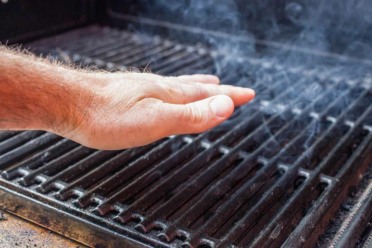 A smoking grill and a hand over it checking its heat output 