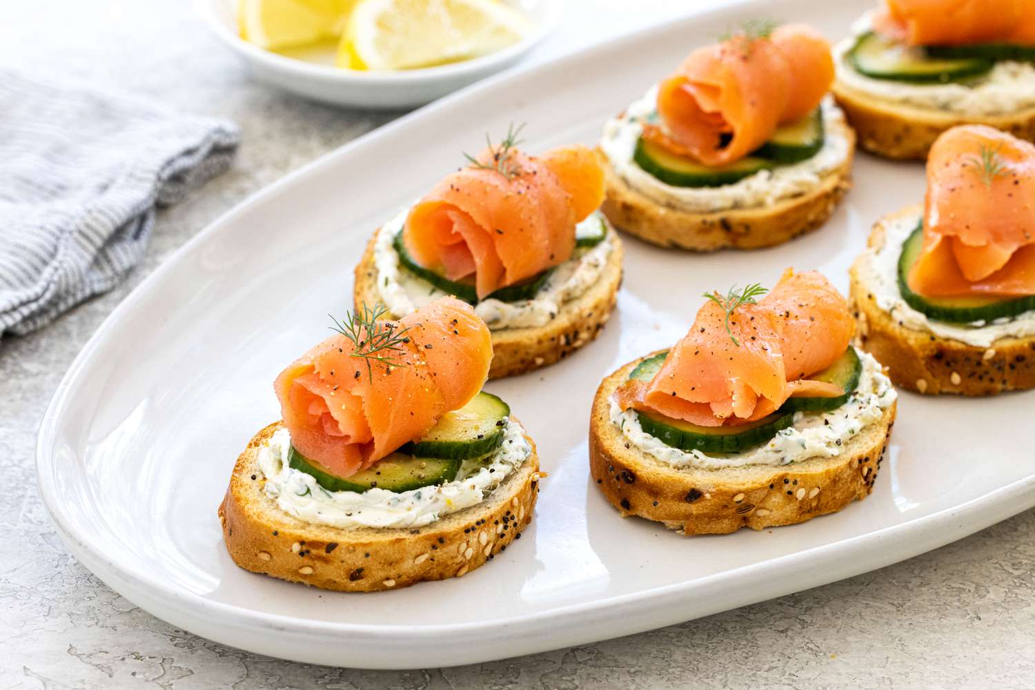 Smoked salmon, cucumber, and cream cheese crostini on a platter.