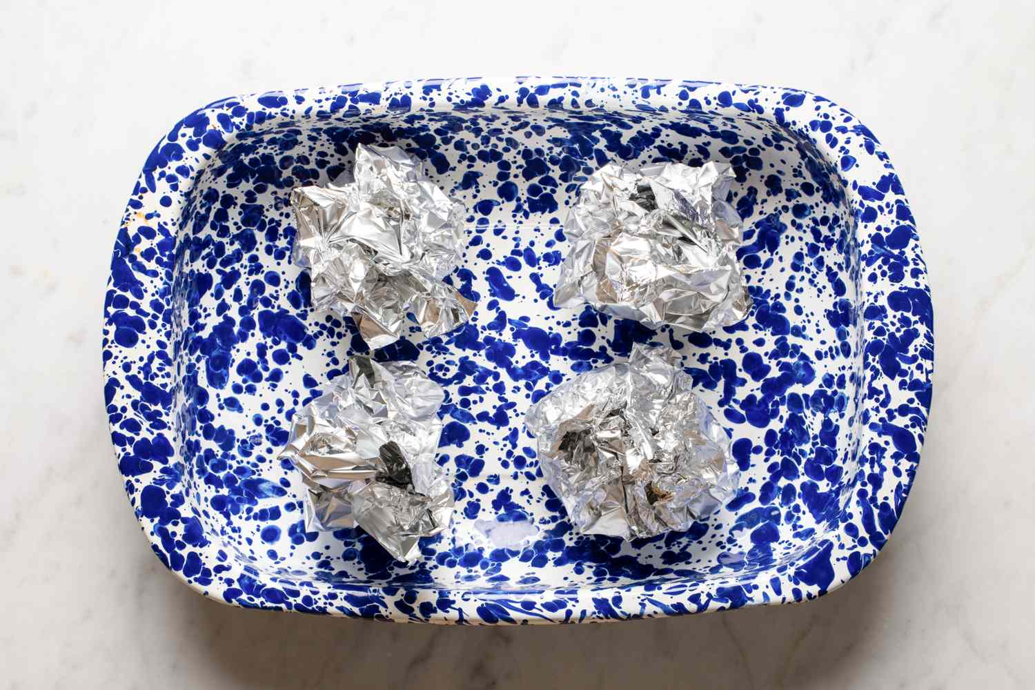 Four foilwrapped items placed in a speckled blue baking dish